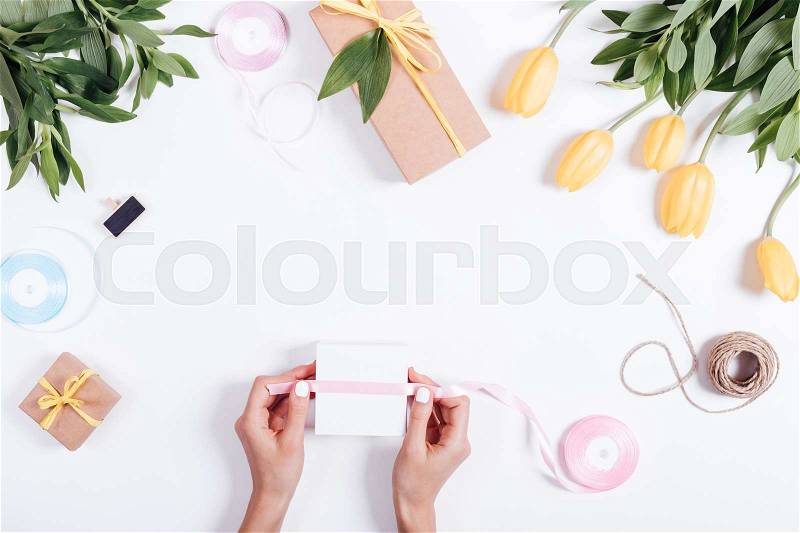 Female hand tied ribbon box with a gift on white table, top view, stock photo