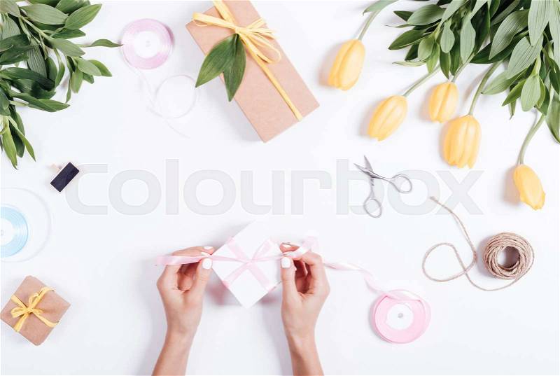 Top view of female hands tie a pink ribbon box with gifts on a white table, stock photo