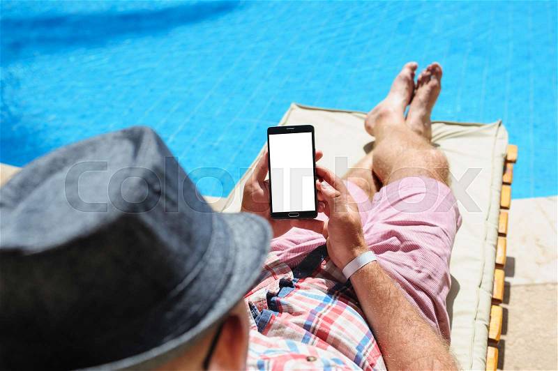 Man in hat sunbathing on the phone by the pool, stock photo