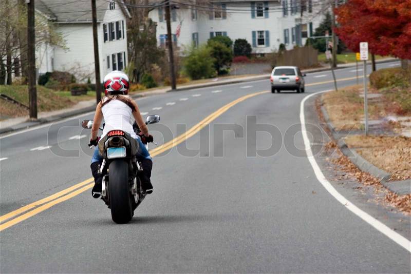 A young woman on a motorcycle maintains a safe following distance with the car ahead, stock photo