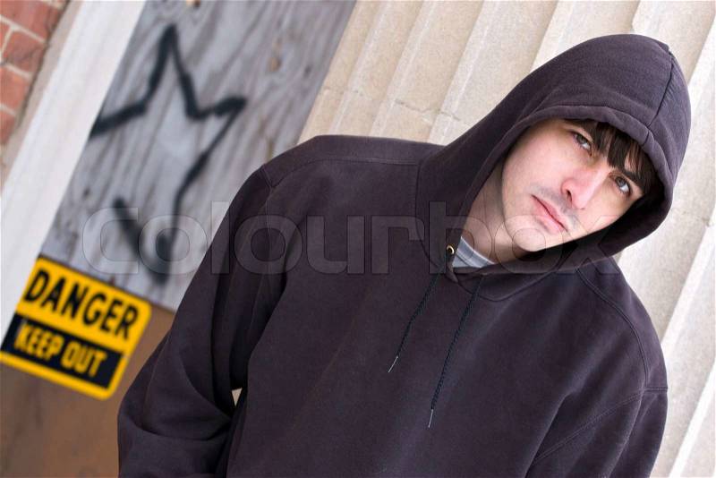 A tough looking guy posing in a grungy urban setting in a hooded sweat shirt, stock photo
