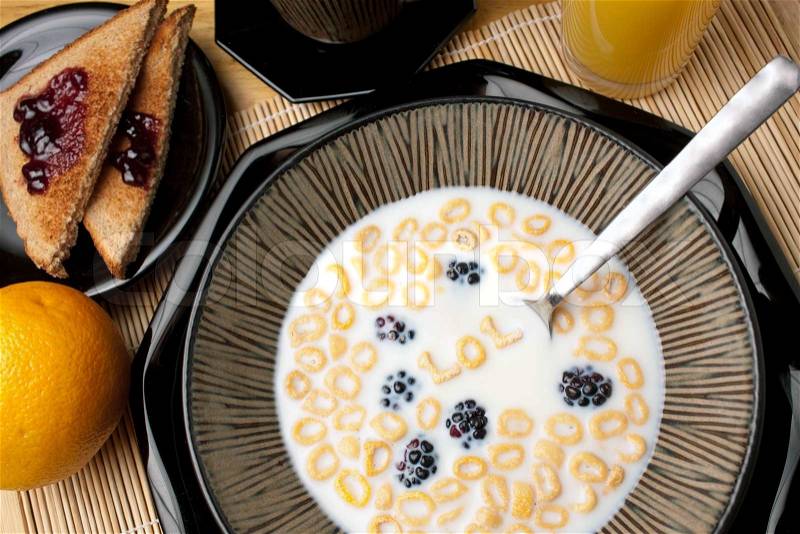 The abbreviation LOL which stands for laughing out loud spelled out of letter shaped cereal pieces floating in a milk filled cereal bowl Surrounding is an orange juice coffee and toast, stock photo