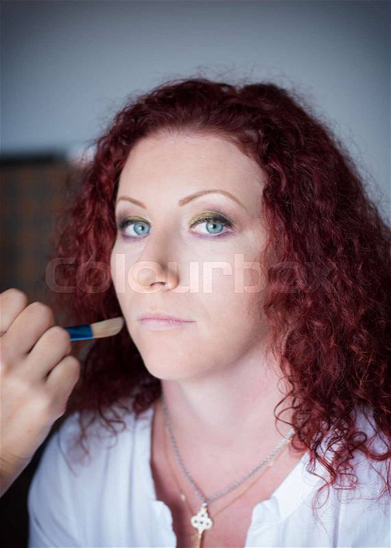 Red-haired lovely girl in a hairdressing salon makes a professional make-up, stock photo