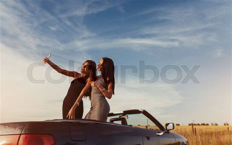 Two sexy brunette woman standing near cabriolet on the road in pitch and pictures to your phone, stock photo