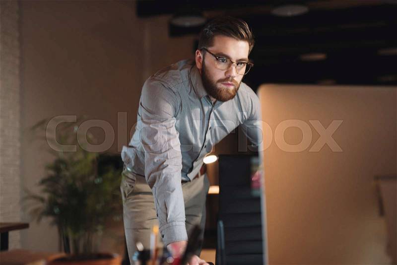 Photo of serious web designer dressed in shirt and wearing eyeglasses working late at night, stock photo