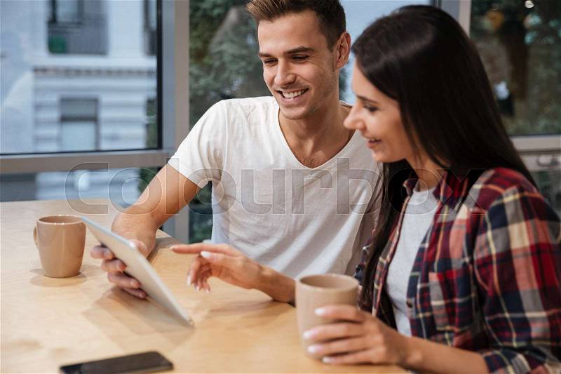 Side view of Young Coworkers sit by the table with coffee and laptop, stock photo