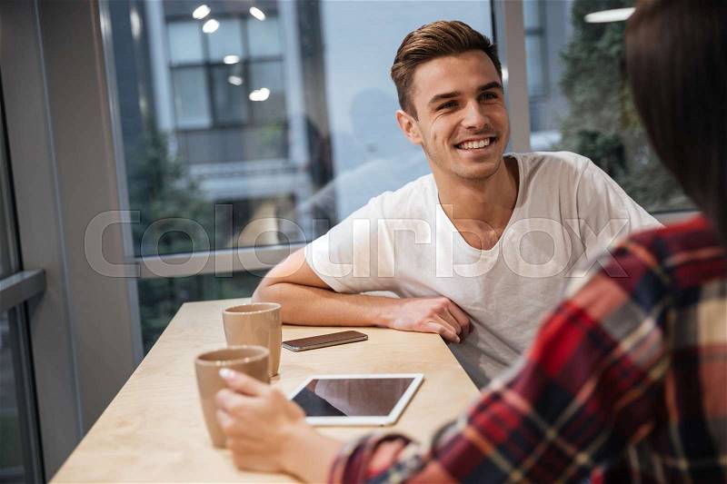 Cropped image of Coworkers sit by the table with coffee and tablet computer. Photo from back of woman, stock photo