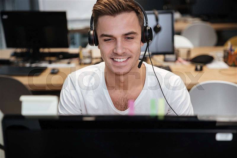 Smiling Man sitting by the computer in headphone in office, stock photo