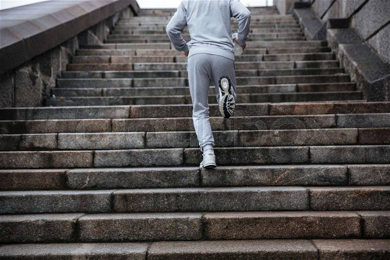 Back view of man in gray sportswear running on stairs. Cropped image, stock photo