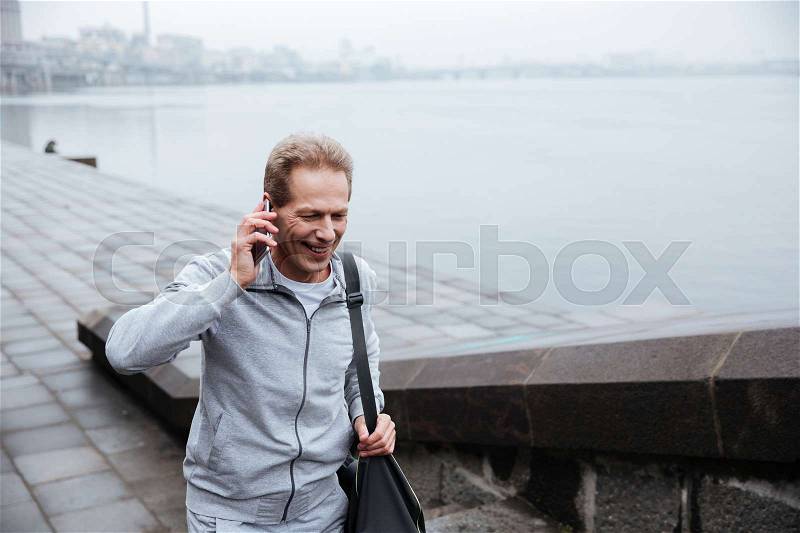Runner in gray sportswear with bag talking at phone and walking on stairs, stock photo