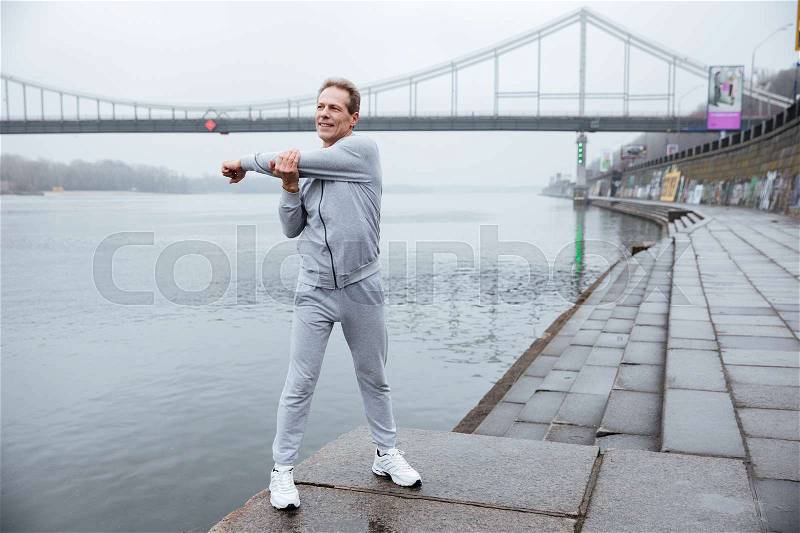 Full length runner in gray sportswear warming up near the river, stock photo