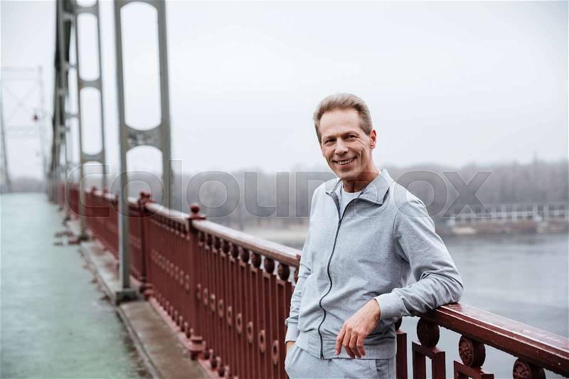 Runner in gray sportswear standing on bridge and looking at camera, stock photo
