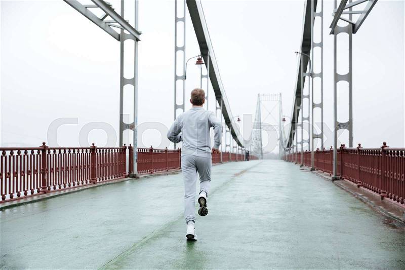 Back view of Man in gray sportswear running on bridge. Full length image, stock photo