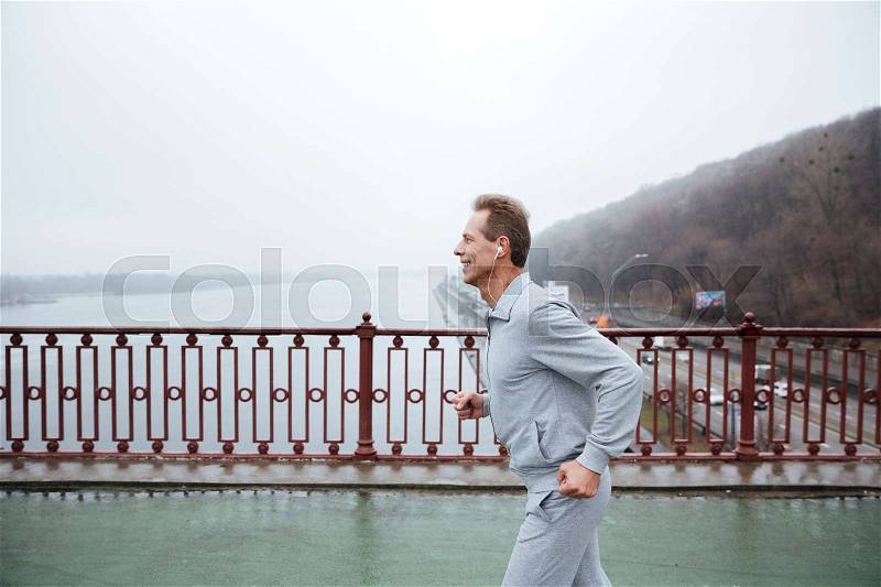 Side view of Man in gray sportswear running on bridge, stock photo
