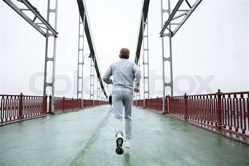 Back view of Elderly Man in gray sportswear running on bridge, stock photo