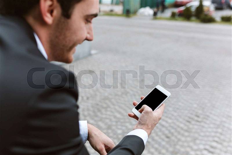 Back view of smiling business man in suit with phone outdoors, stock photo