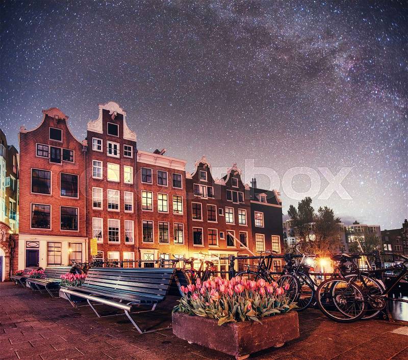 Fantastic starry sky at night in Amsterdam. Beautiful illumination of buildings near the water in the channel. Art photography, stock photo