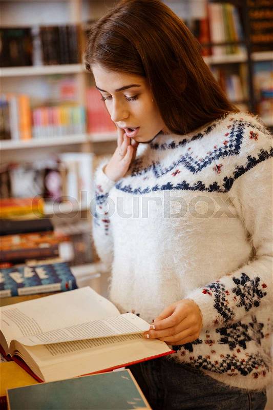 Portrait of a surprised young woman reading book in library, stock photo