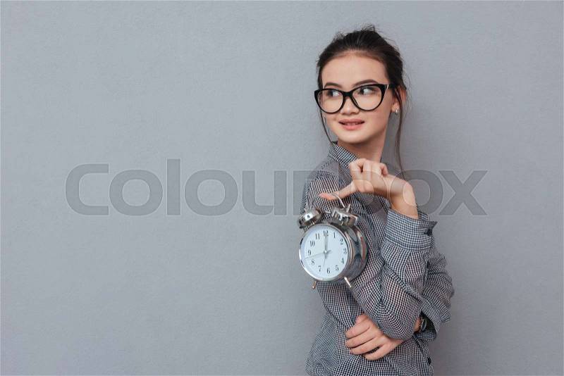 Side view of asian woman in glasses posing with clock and looking back. Isolated gray background, stock photo