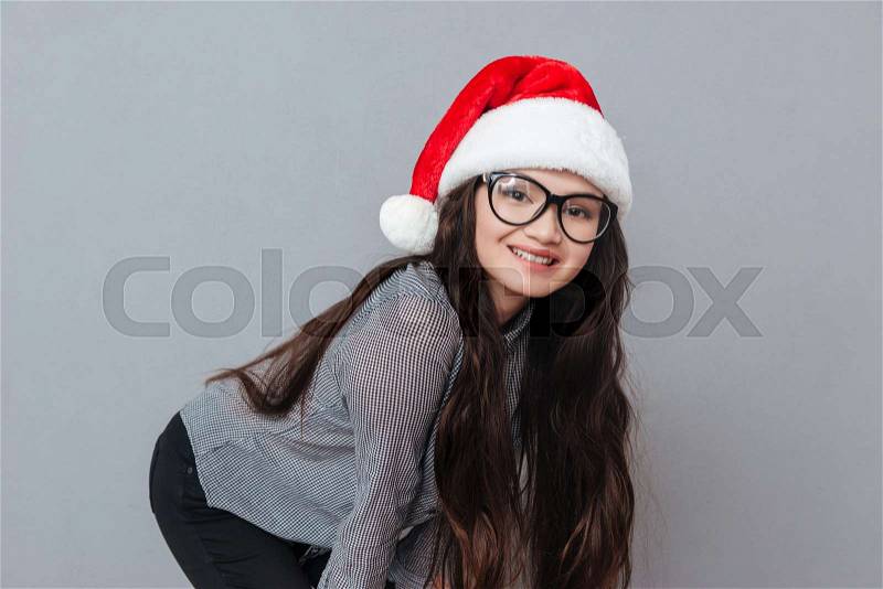 Happy Asian woman in christmas hat posing in studio and looking at camera. Isolated gray background, stock photo