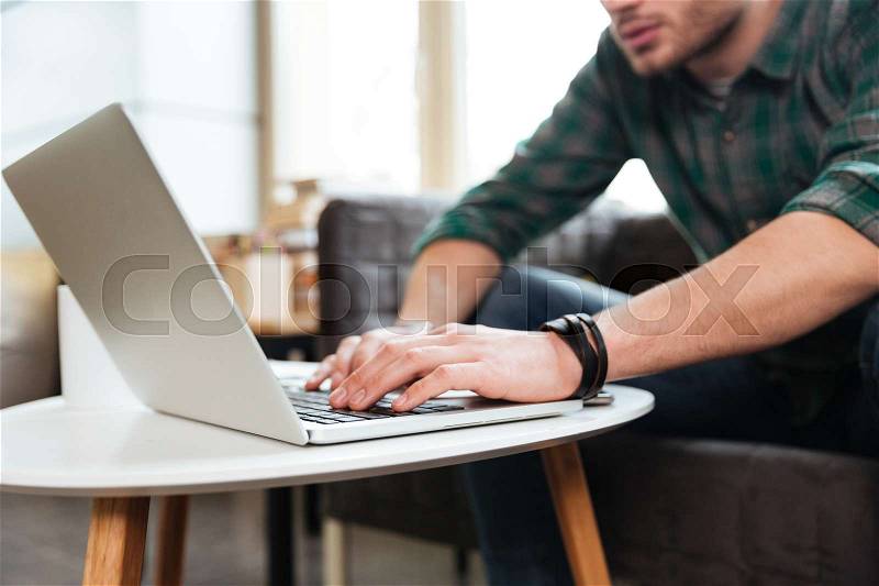 Cropped image of man in green shirt sitting with laptop by the table. Focus on laptop. Side view. Coworking, stock photo