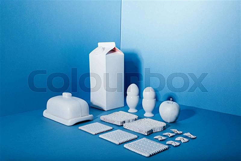 White pack of milk, eggs, butter, apple and cookies over blue background, stock photo