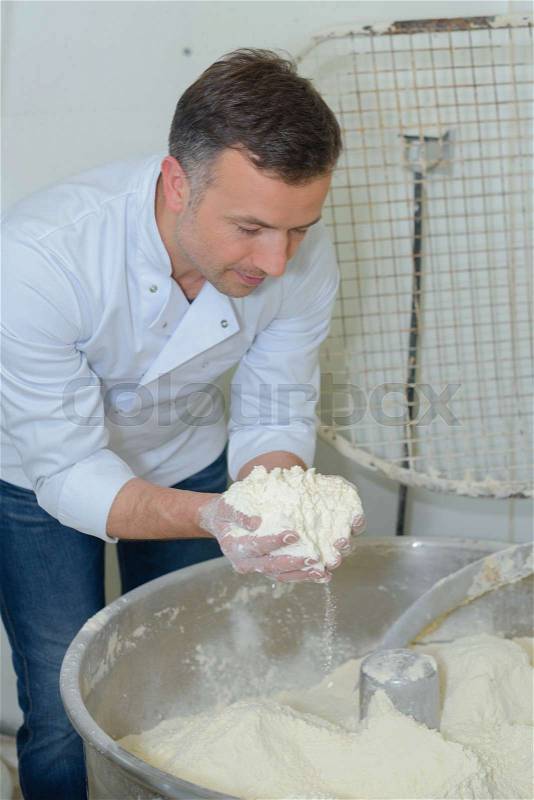 Chef with handful of flour over industrial mixer, stock photo