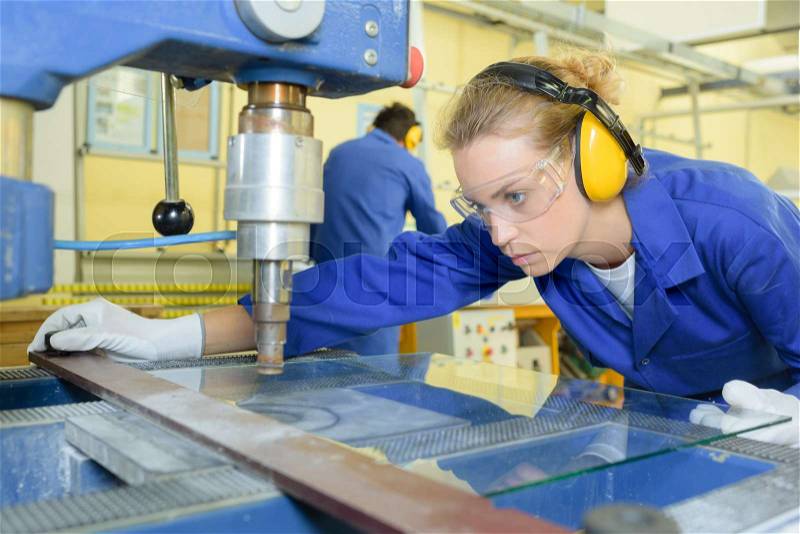 Serious trainees focused on drilling metal piece with professional machinery, stock photo