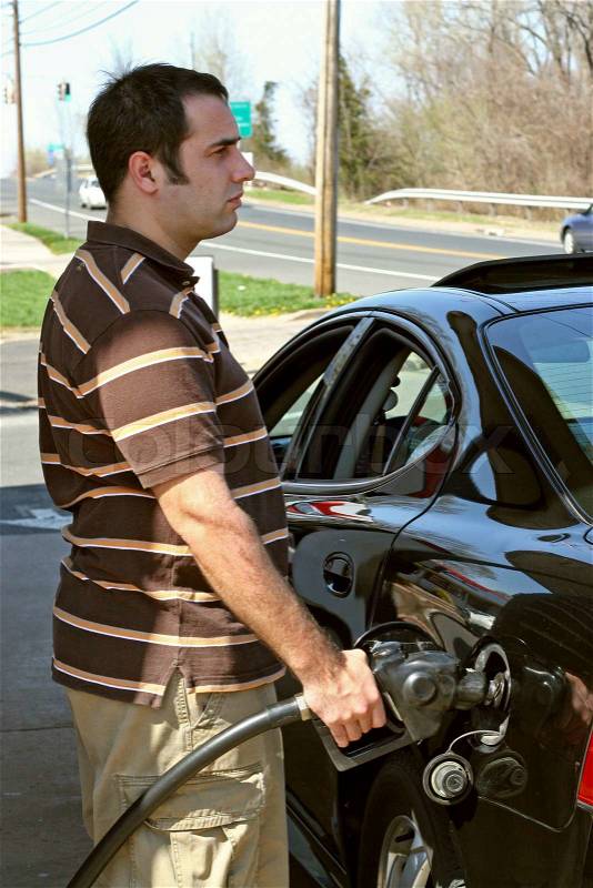 A man pumping high priced gas into his car with a disgusted look on his face, stock photo