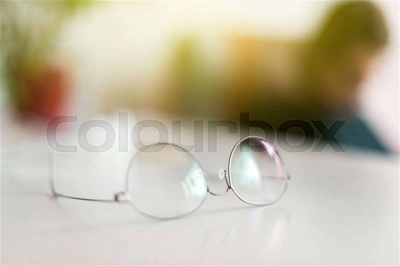 Elegant eyeglasses spectacles with thin titanium rim on office table with office employee silhouette working in the background, stock photo