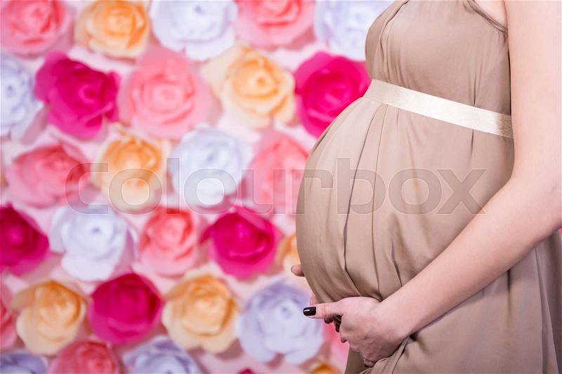 Pregnant woman\'s belly over colorful paper flowers background, stock photo
