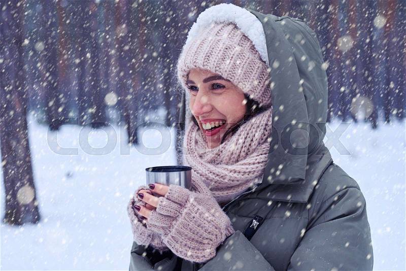 Side view shot of beautiful young woman in pink knitted cap, scarf, and mittens holding a cup of hot tea. Holidays concept , stock photo