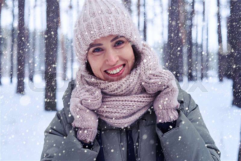 Elated female enjoys winter. Woman under snowfall looking at the camera outside on snowing cold winter day. Portrait Caucasian female model outside in first snow, stock photo