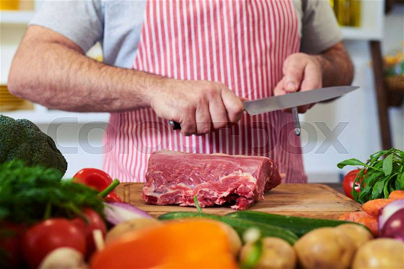 Crop shot of hands sharpening knife for cutting meat over working desk. Rack focus on vegetables. Fresh, raw vegetables lying on the board , stock photo