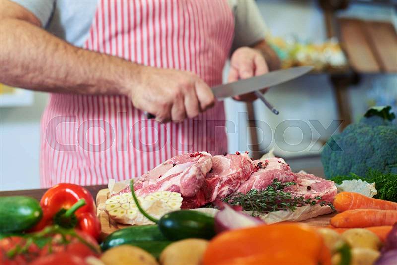 Crop shot of hands sharpen knife. Preparing lean meat. Hands of a man preparing meat and vegetables in a kitchen. Focus on hands, vegetables lying on the table , stock photo