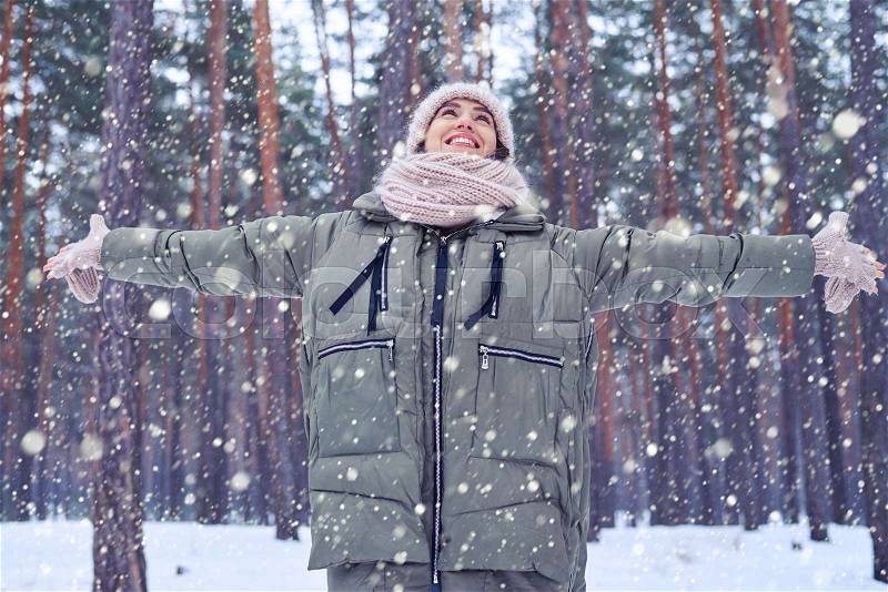 Low angle of happy and smiling woman looking at the sky while standing in the forest. Winter is coming. Having fun on a cold sunny day. Catching snowflakes in winter, stock photo