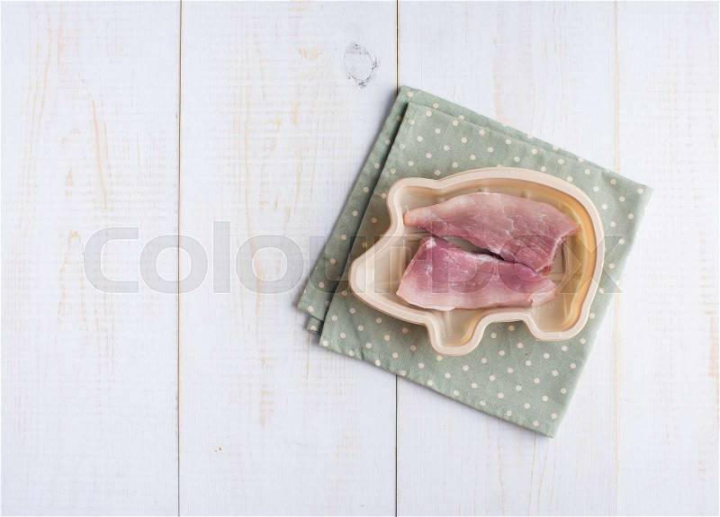 Bowl of pig shape with raw pork tenderloin on wood, stock photo