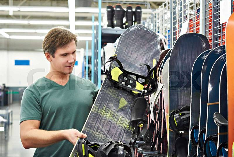 Man chooses a snowboard in sport store, stock photo