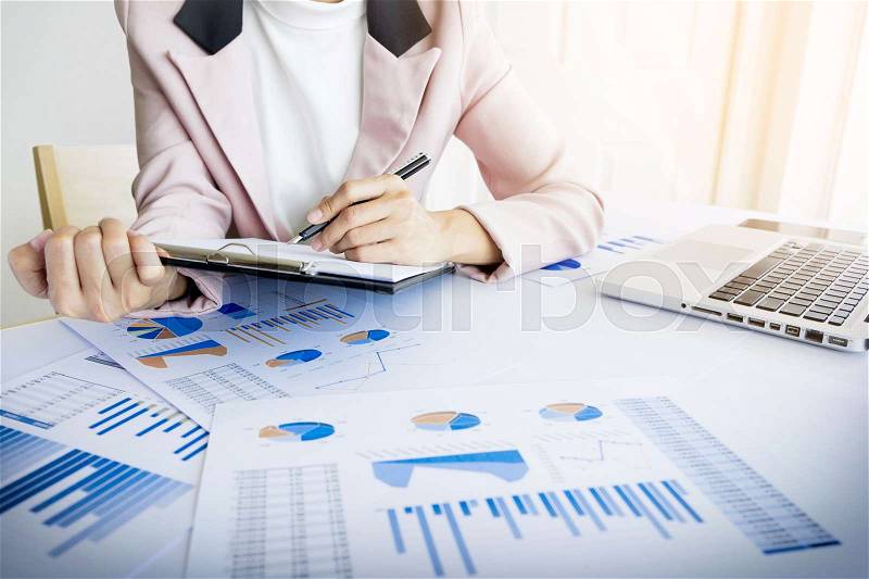 Portrait of business woman with laptop, finance graph and writes on a document at her office, stock photo