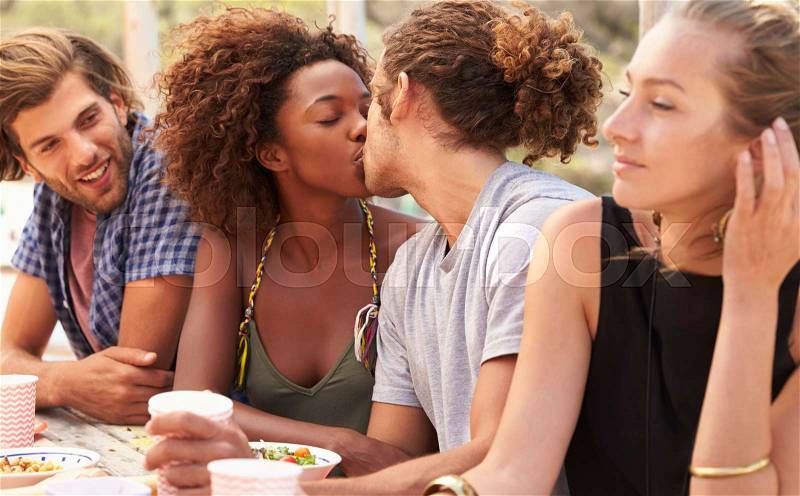 Four friends at a table by the sea, couple kissing, close up, stock photo