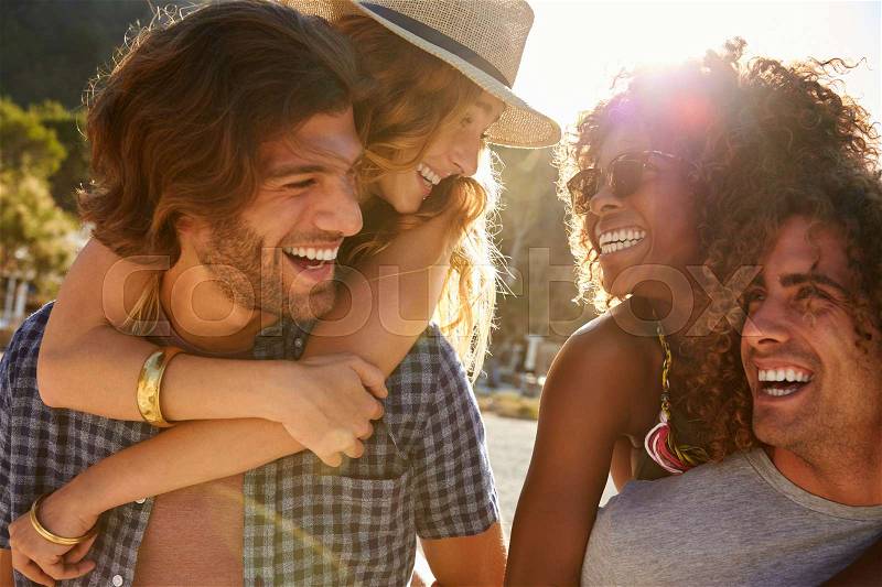 Two couples piggybacking at the beach, looking at each other, stock photo