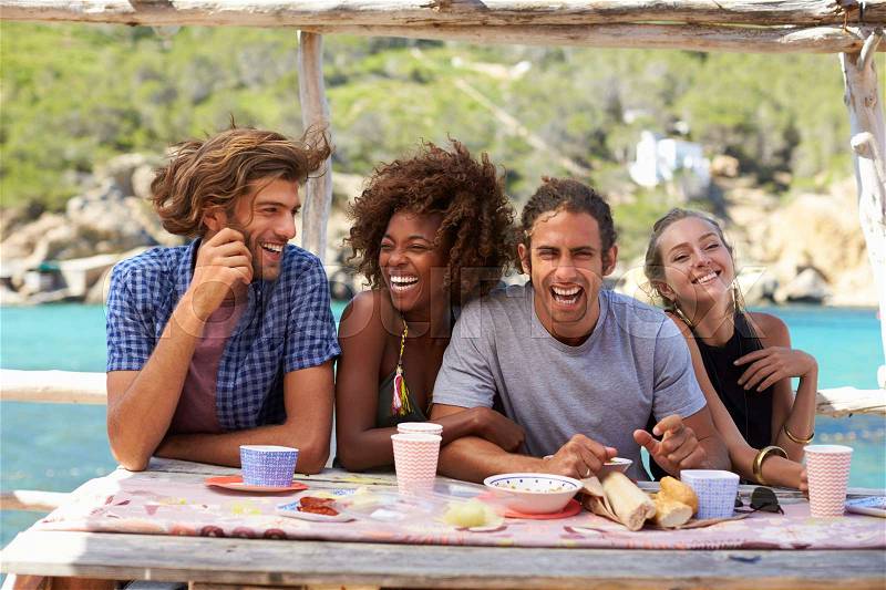 Four friends at a table by the sea looking to camera, Ibiza, stock photo