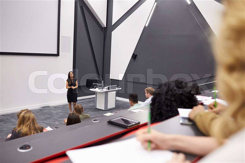 Woman lecturing students in a lecture theatre, mid row POV, stock photo