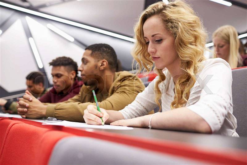 Female student taking notes in a university lecture theatre, stock photo