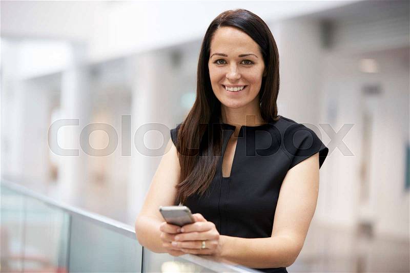 Young woman holding phone in modern university interior, stock photo