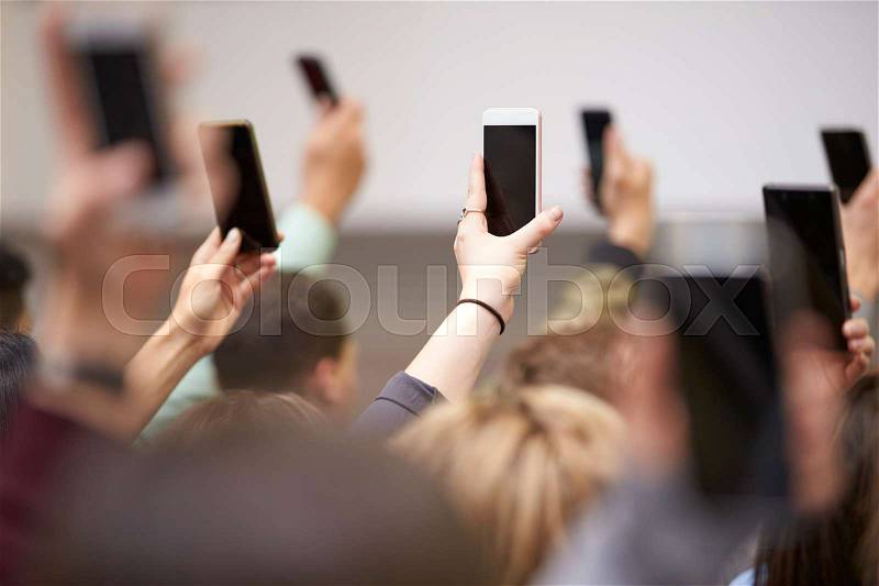 Hands in a crowd holding phones up to take pictures, stock photo