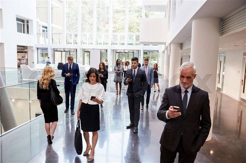 Businesspeople Using Technology In Busy Lobby Area Of Office, stock photo
