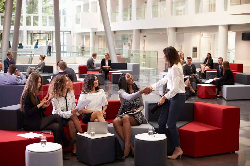 Businesswomen Meeting In Busy Lobby Of Modern Office, stock photo