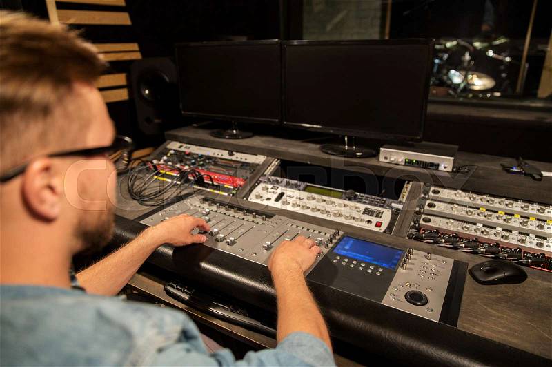 Music, technology, people and equipment concept - man at mixing console in sound recording studio, stock photo