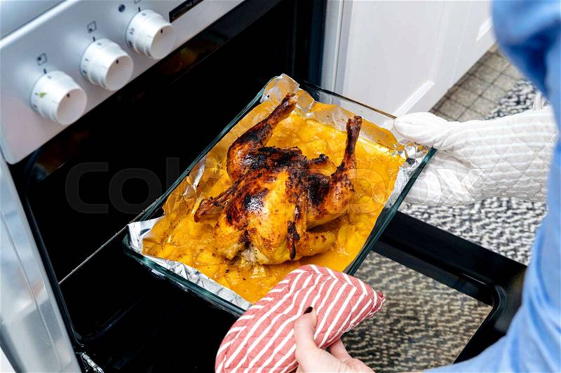 Delicious roasted chicken out of the oven by woman hands wearing protection glove made under special Swedish recipe with ginger, oranges, apples and other organic food ingredients - ready to be served, stock photo